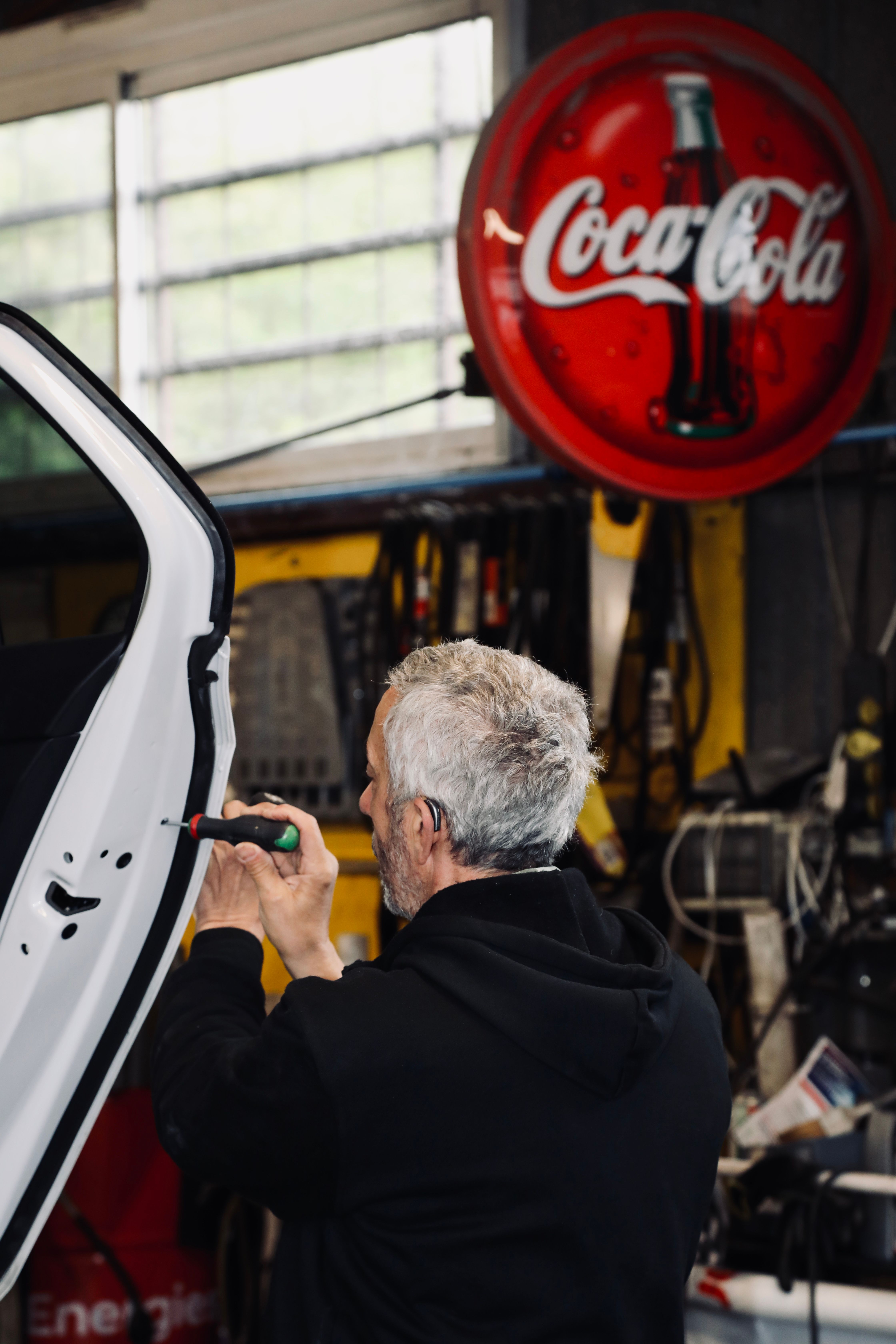 Mechanic Working in Garage with Coca-Cola Sign · Free Stock Photo