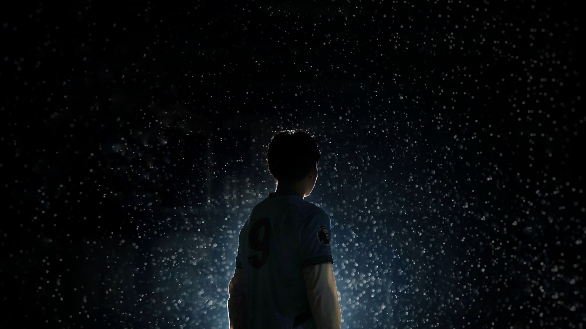 Athlete silhouette standing in rain under stadium light wearing an Awaline custom kit