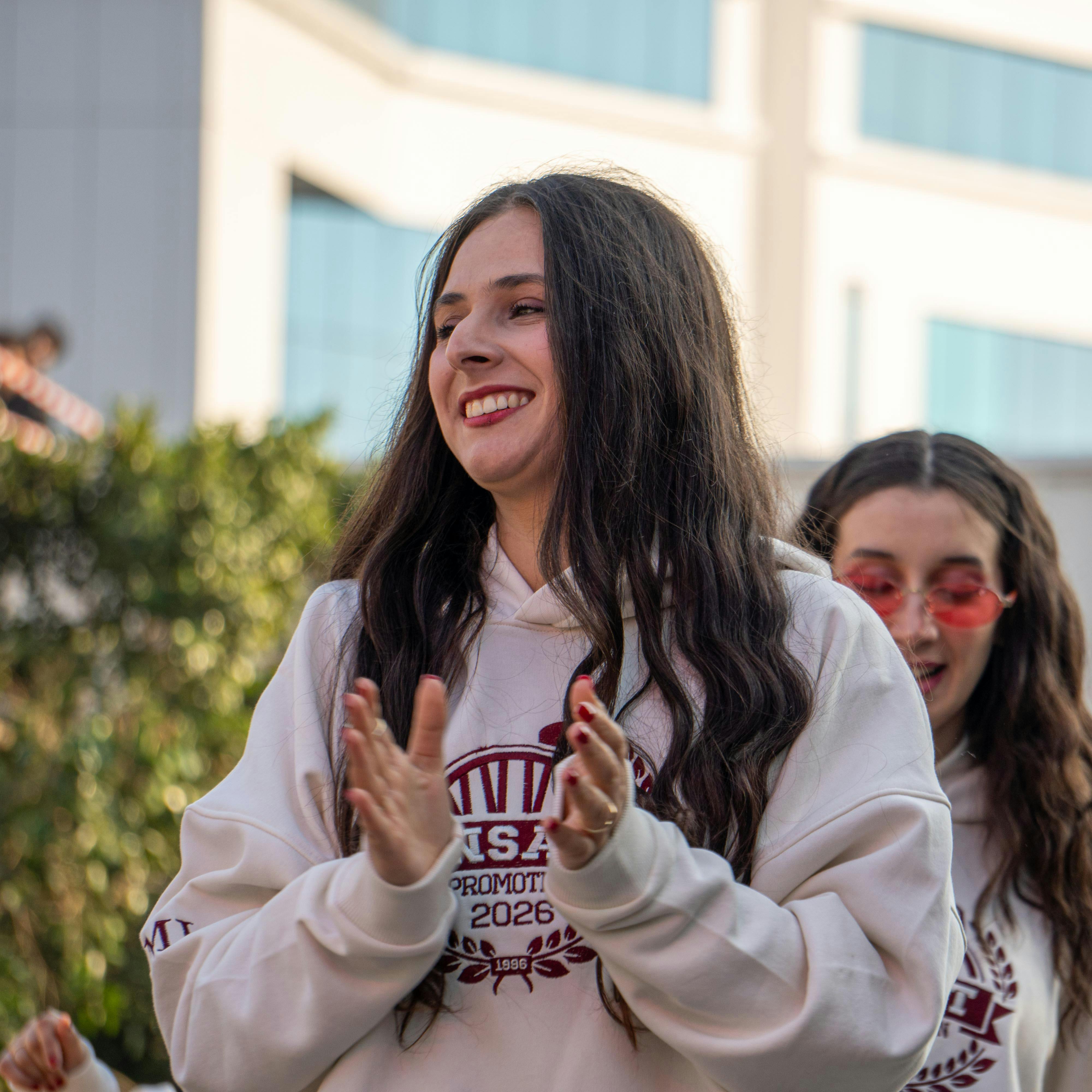 Two young women outdoor, clapping and smiling, enjoying a sunny day together.