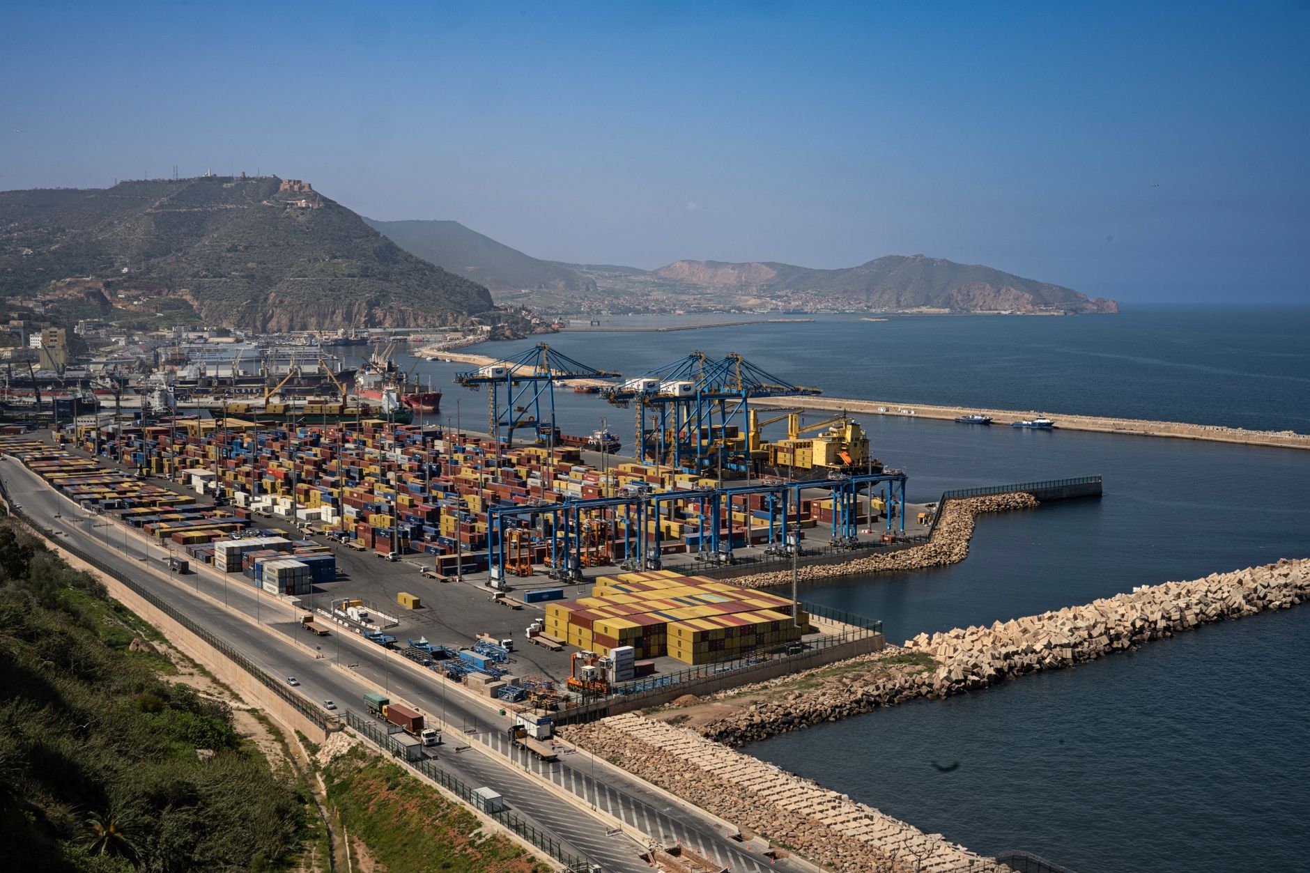 Port of Oran showing containers, cranes, and Algerian coastline in the background.