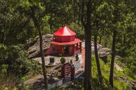 A charming red temple nestled among pine trees in Binsar, Uttarakhand, India, during a sunny day.