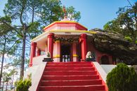 A beautiful Hindu temple surrounded by pine trees in Binsar, Uttarakhand, India, under a clear blue sky.