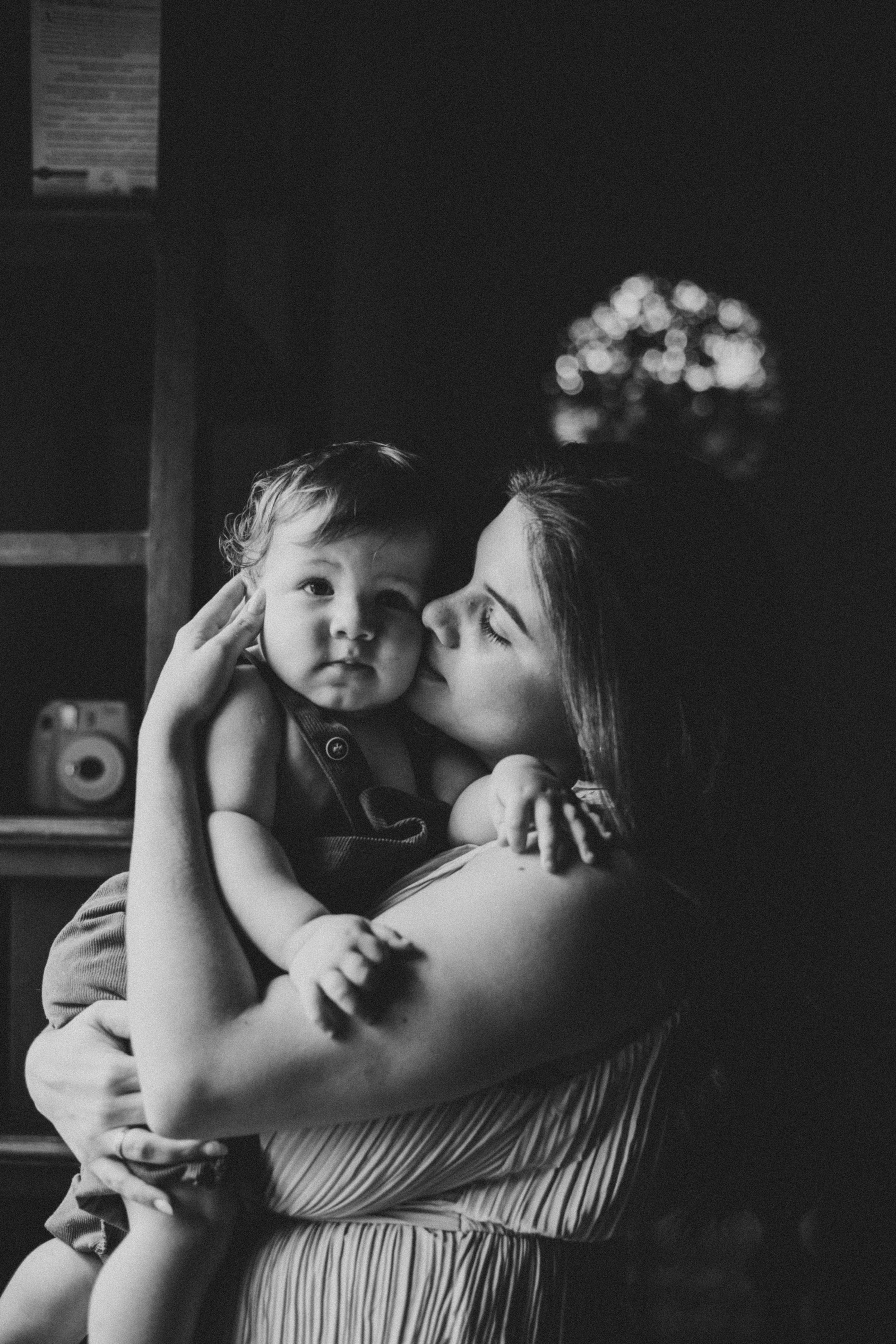 Heartwarming black and white photo of a mother kissing her baby indoors.