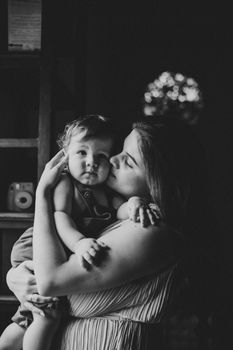 Heartwarming black and white photo of a mother kissing her baby indoors.