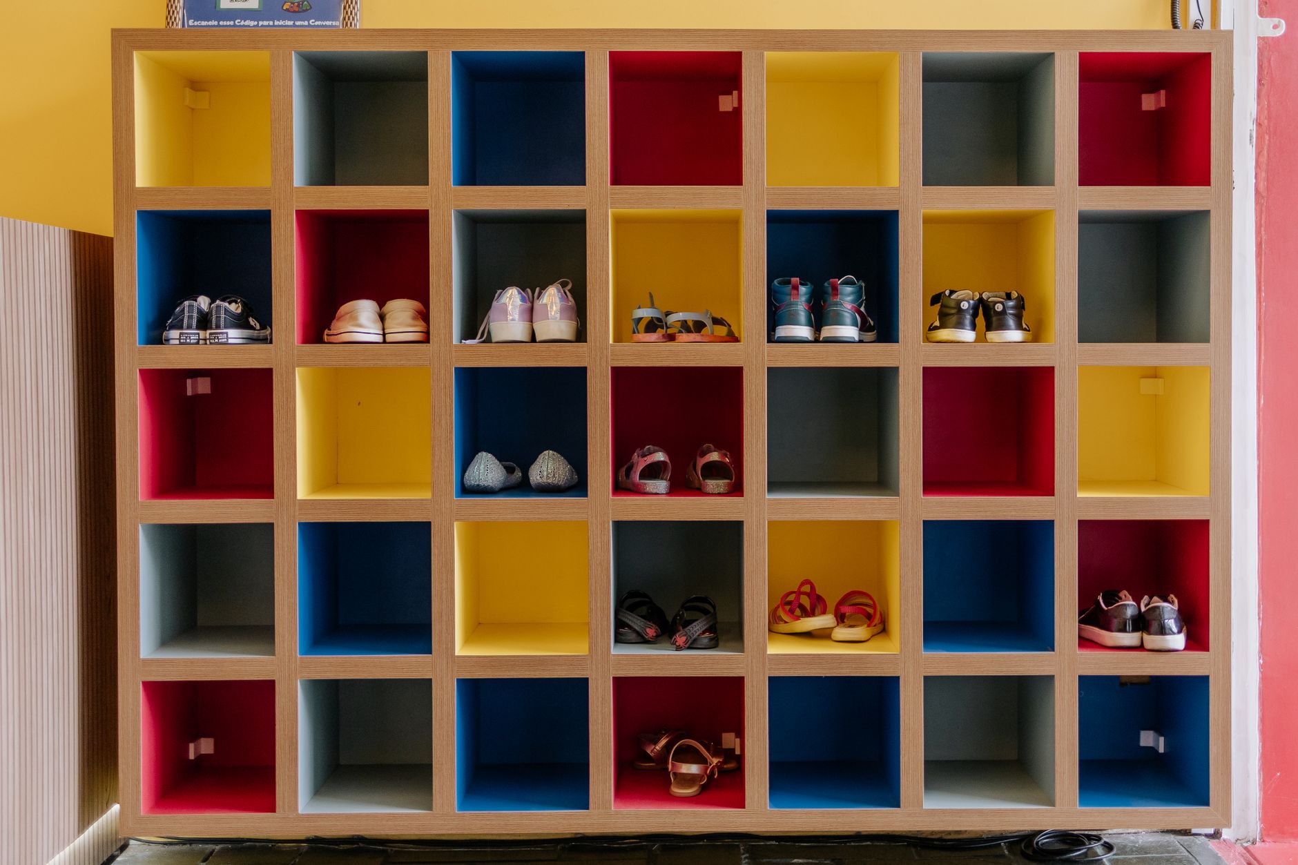 Vibrant cubical shoe cabinet with multicolored boxes displaying various footwear indoors.