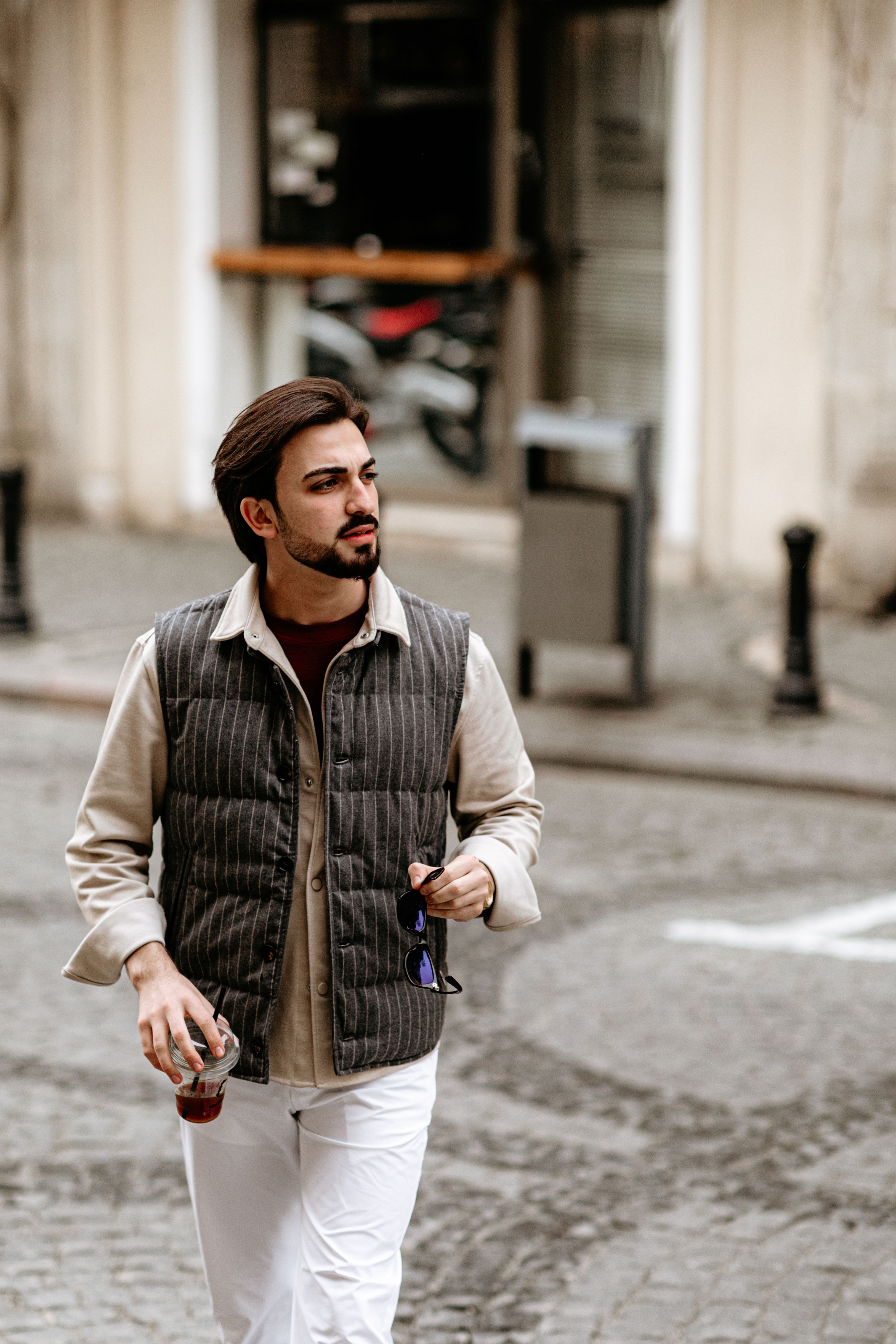Stylish adult male walking confidently through a city street holding a beverage.