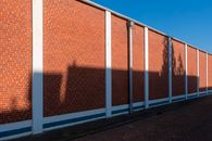 A long red brick wall with geometric shadows cast under clear blue sky.