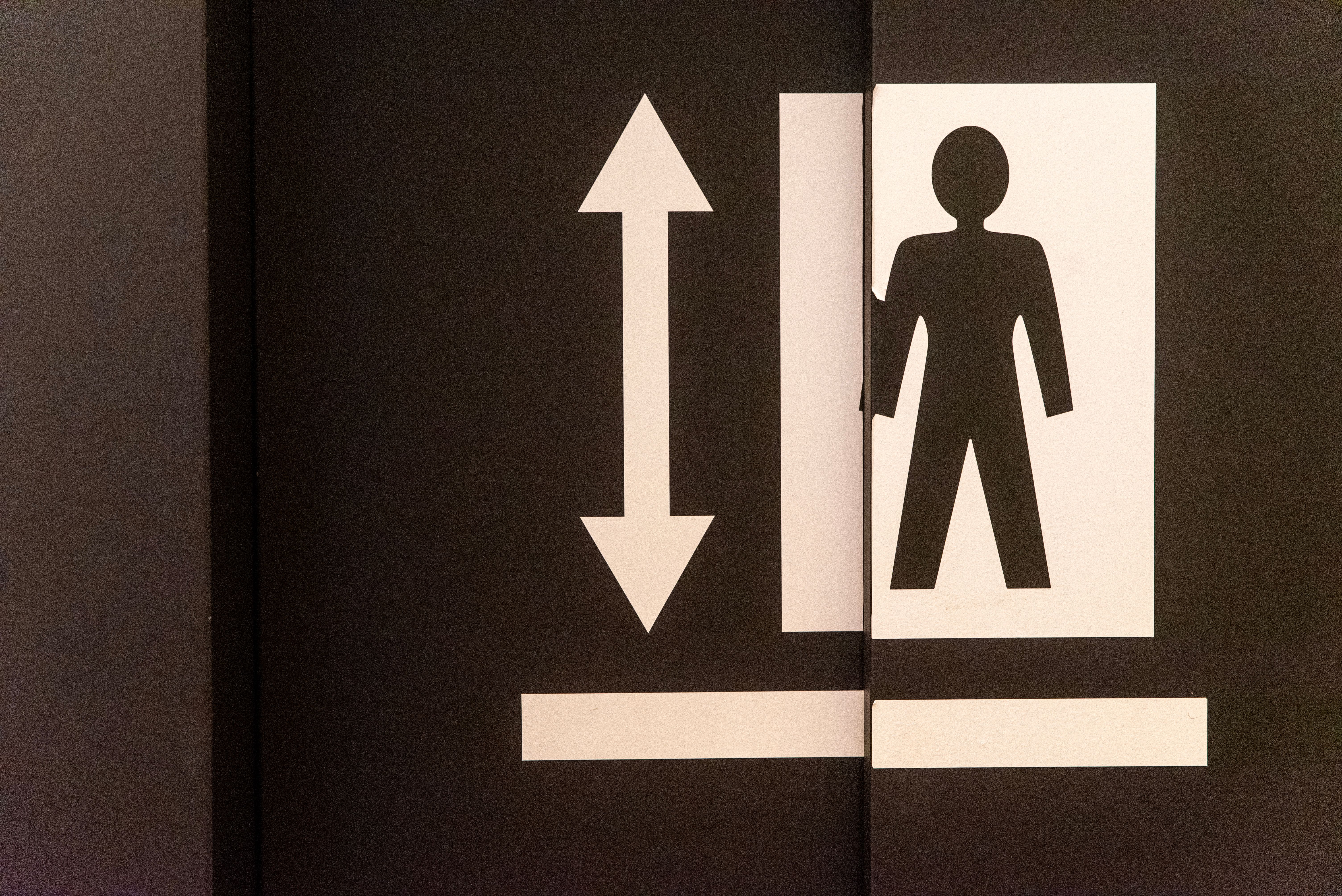 Graphic of an elevator door with a human figure and directional arrow symbol.