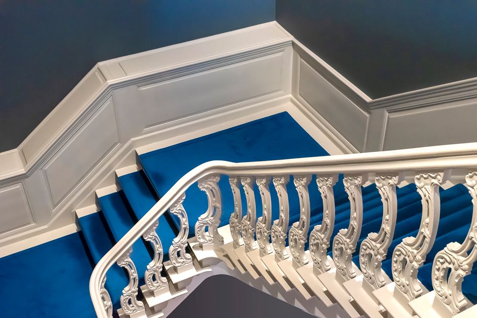 A beautifully detailed white staircase adorned with a vibrant blue carpet in an indoor setting.