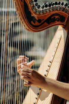 Detailed image of hands playing a harp outside, capturing the instrument's artistry and craftsmanship.