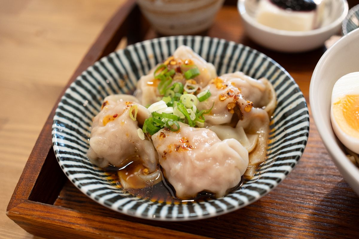 Silky pork wontons in dark chili vinegar sauce topped with scallions in a striped bowl