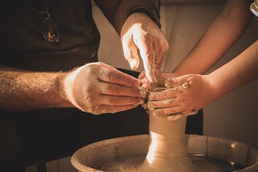 Adult and child hands working together shaping clay on a pottery wheel. Artistic collaboration in a warm, cozy setting.