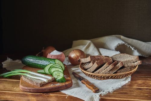 Free A rustic still life of sliced bread, cucumber, onion, and spring onion on a wooden table. Stock Photo