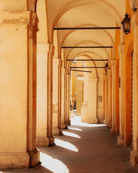 Sunlit arcades with arches in Modena, Italy, showcasing classic Italian architecture.