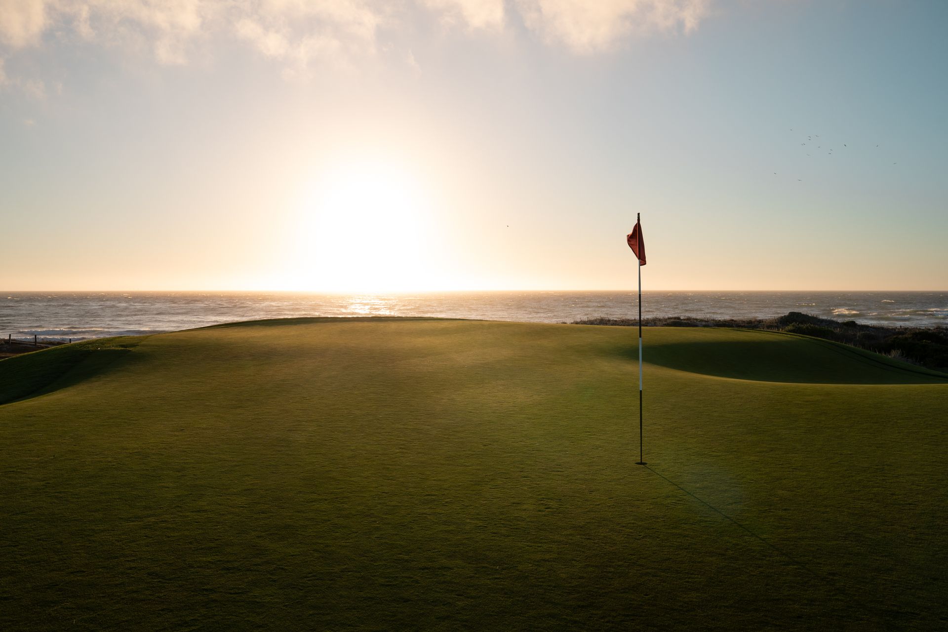 Serene golf putting green with flag at sunset over ocean