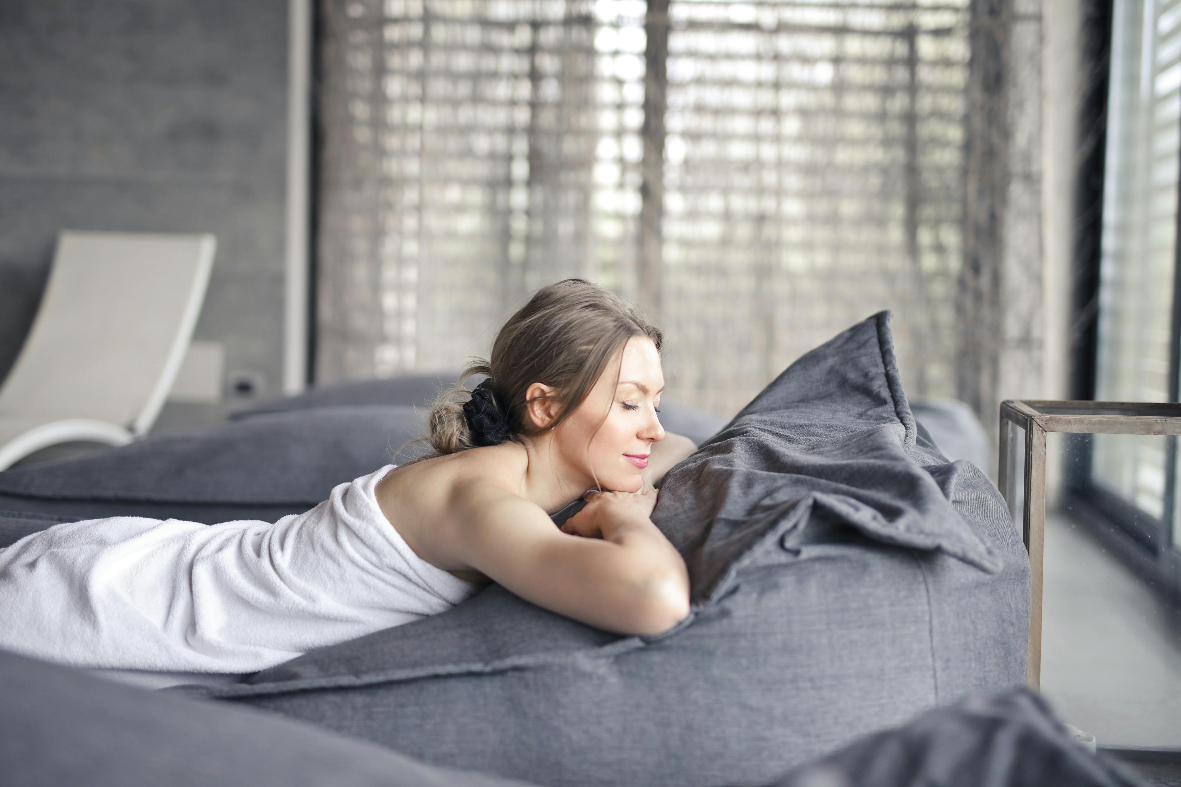 woman in white tank top lying on gray bed