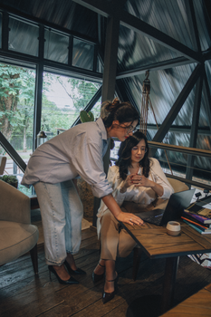 Two women collaborating in a modern office space with a laptop.