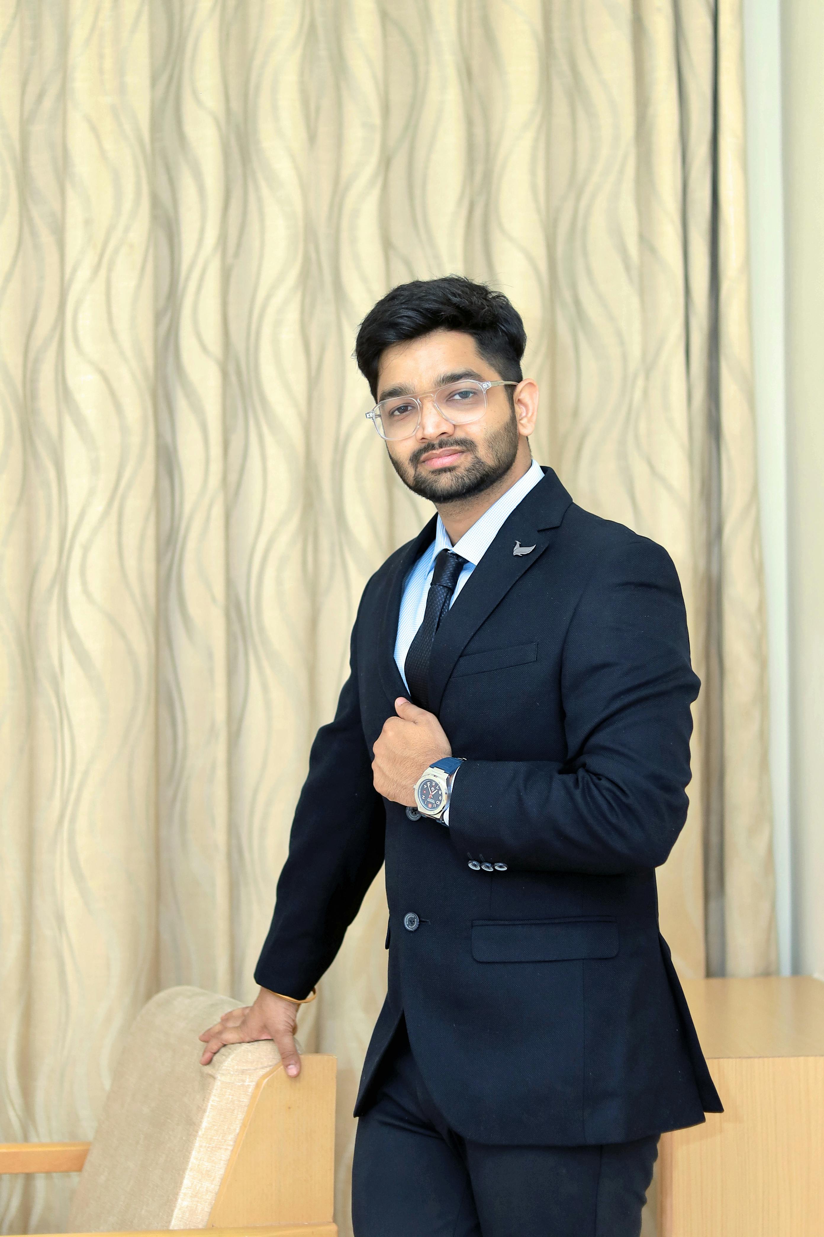 Stylish man in a black suit and tie posing confidently indoors, showcasing modern fashion.
