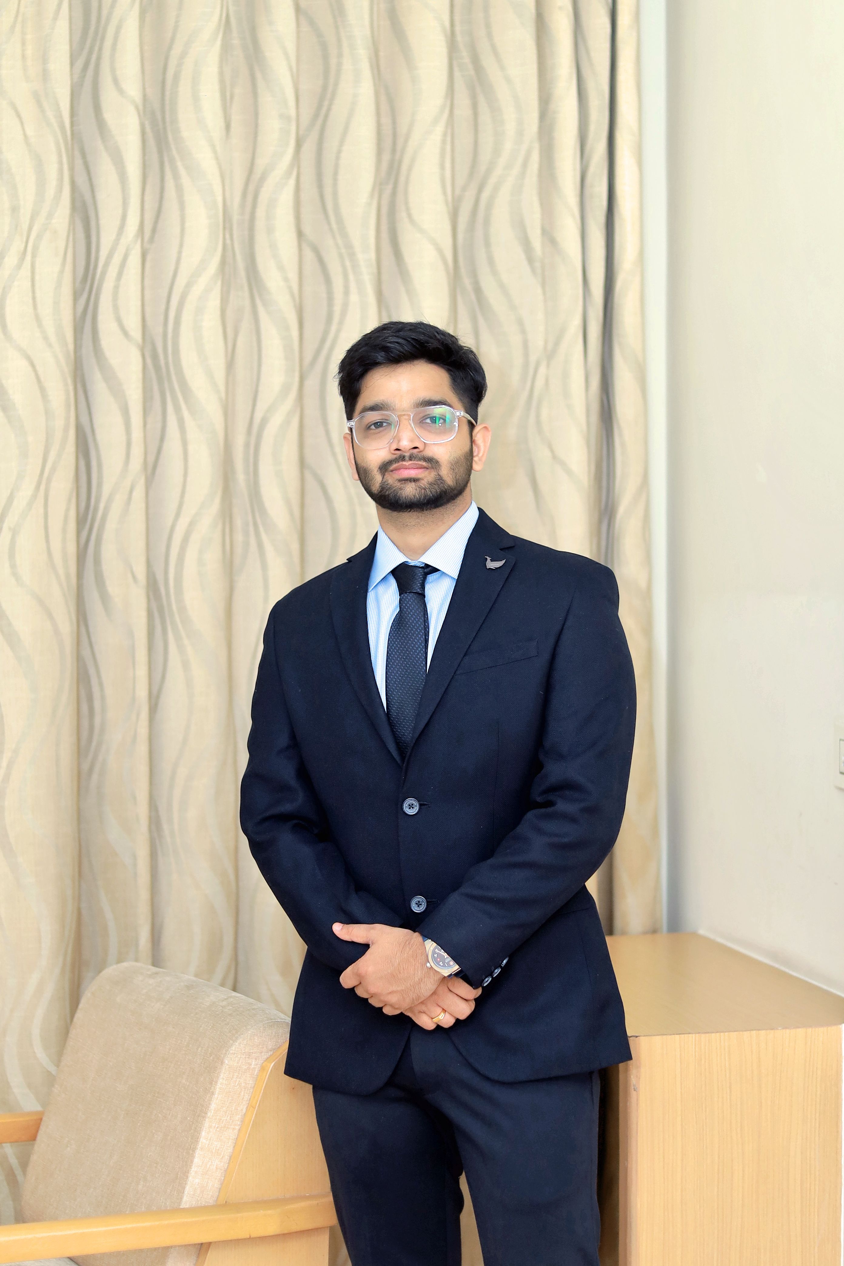 Portrait of a well-groomed man in a black suit standing indoors with a confident smile.