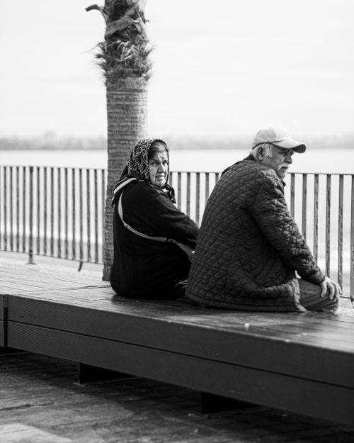 Free A senior couple sitting on a bench by the waterfront, enjoying a peaceful day outdoors. Stock Photo