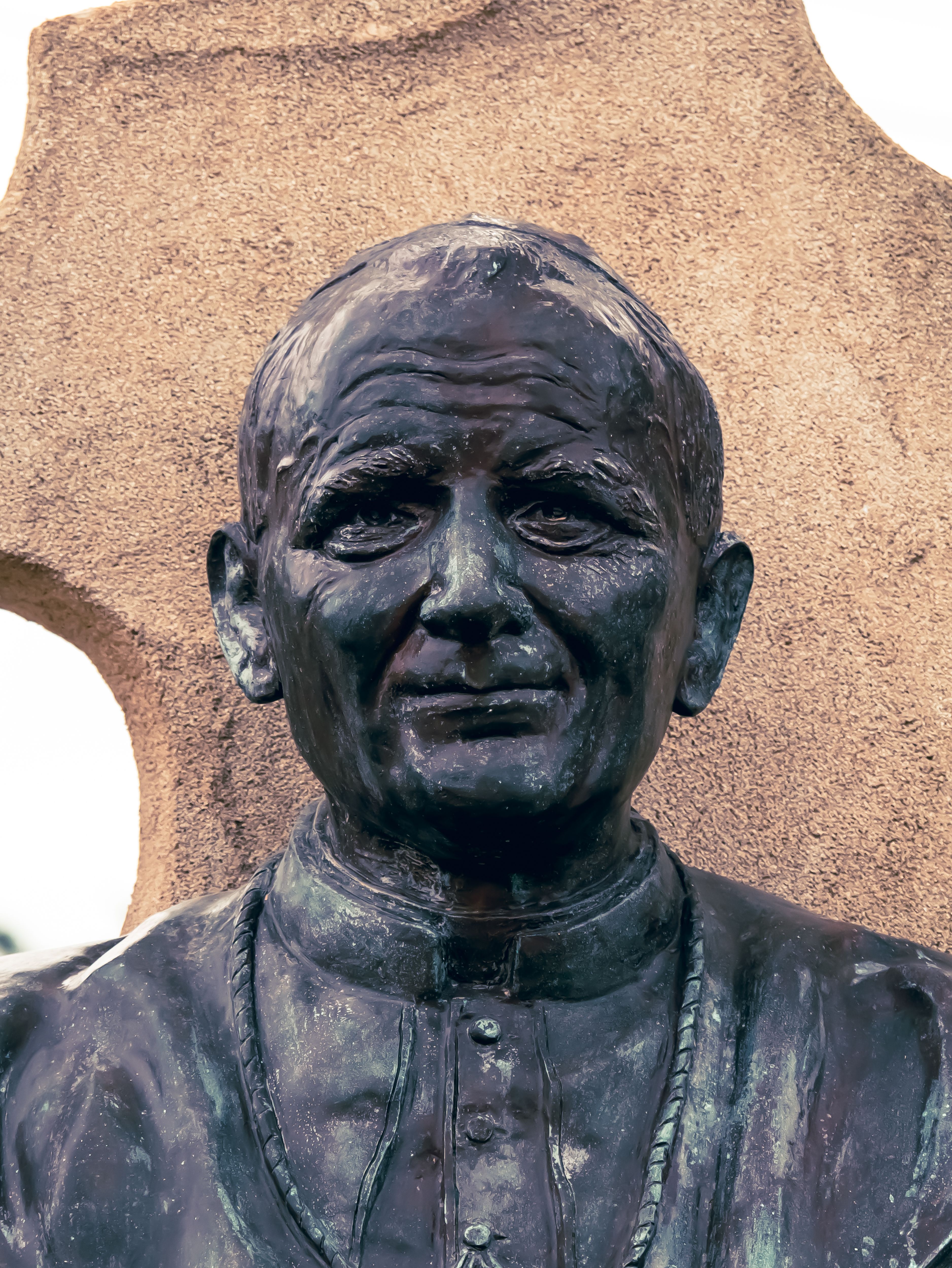 Close-up of a bronze statue depicting a religious figure in traditional attire, set against a stone backdrop.