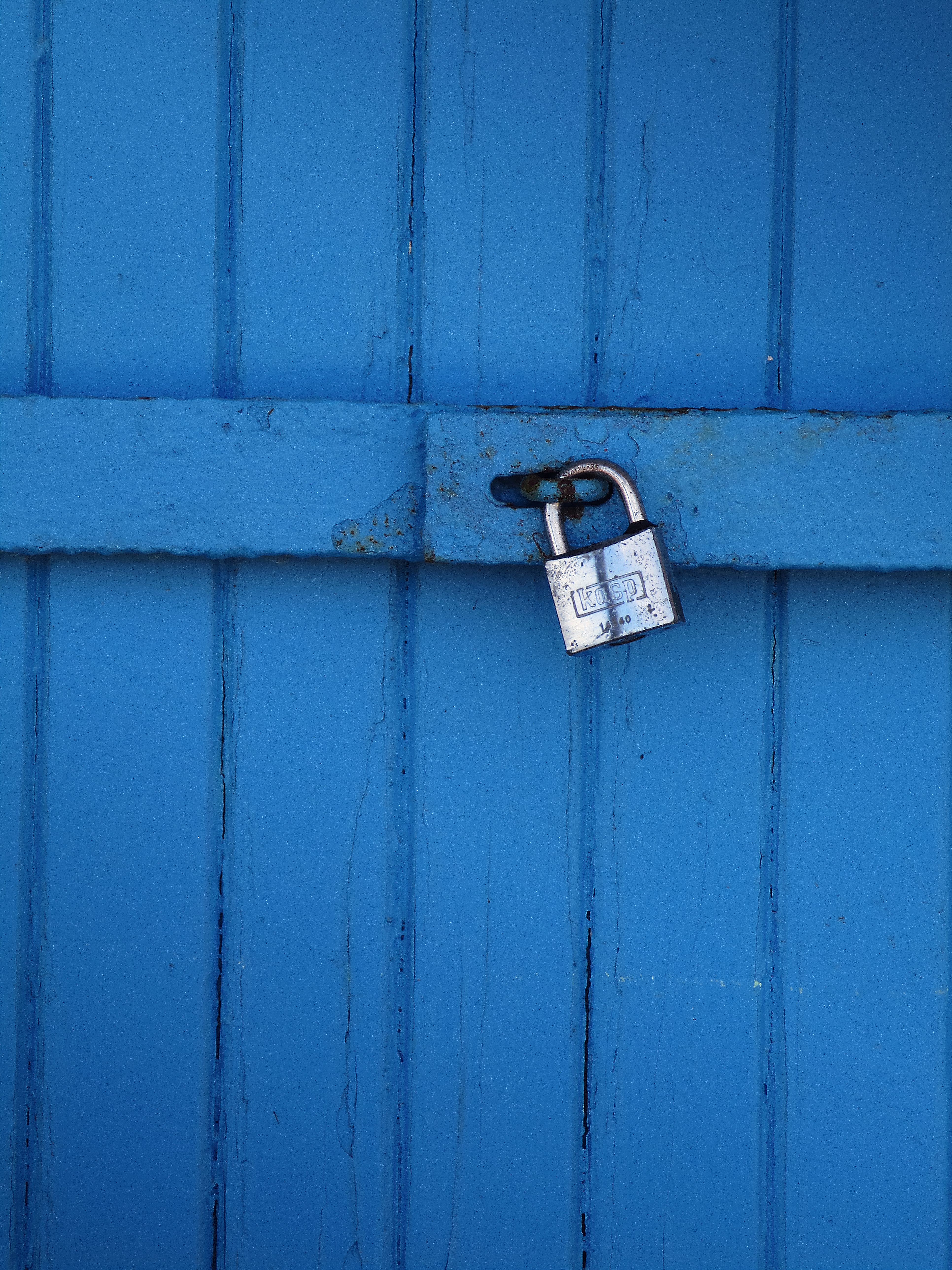 Close-up of a secured blue wooden door with a silver padlock highlighting security and simplicity.