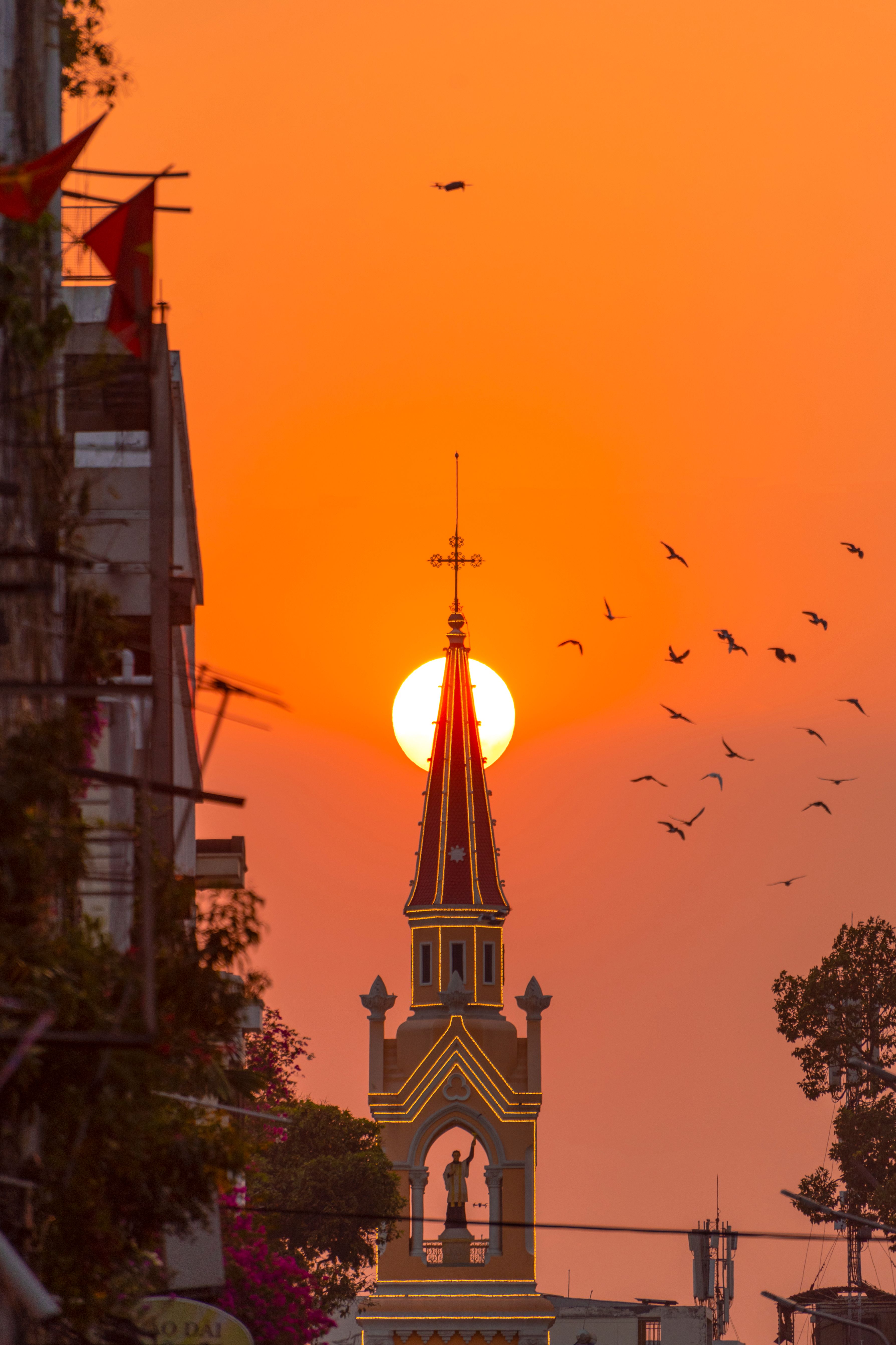 Beautiful Saigon sunset with birds flying over a church spire. Captures the serene essence of Vietnam's architecture.