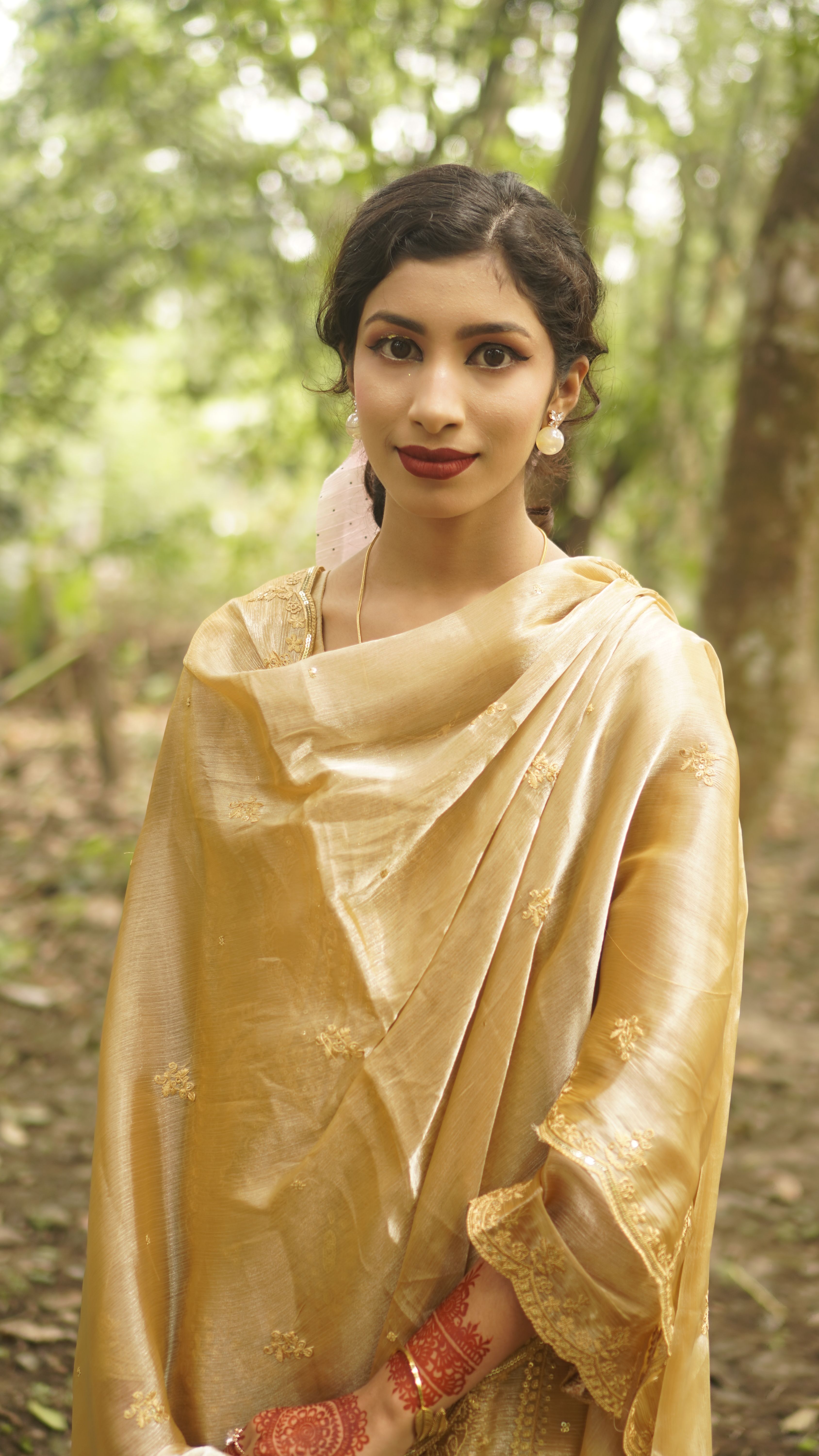 Elegant portrait of a woman in golden traditional attire set against a lush outdoor background.