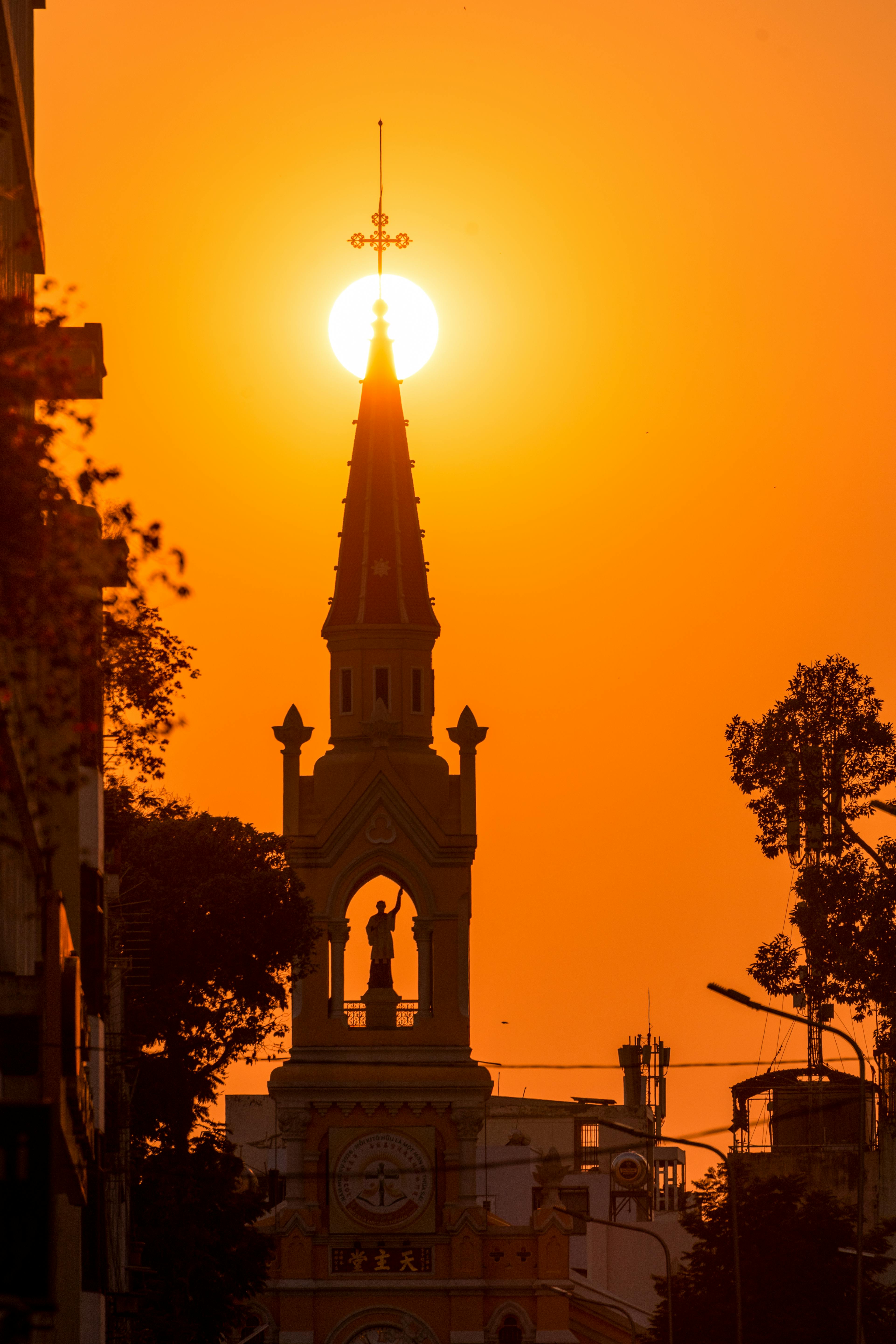 Dramatic silhouette of a church spire in Ho Chi Minh City at sunset, capturing vibrant orange hues.