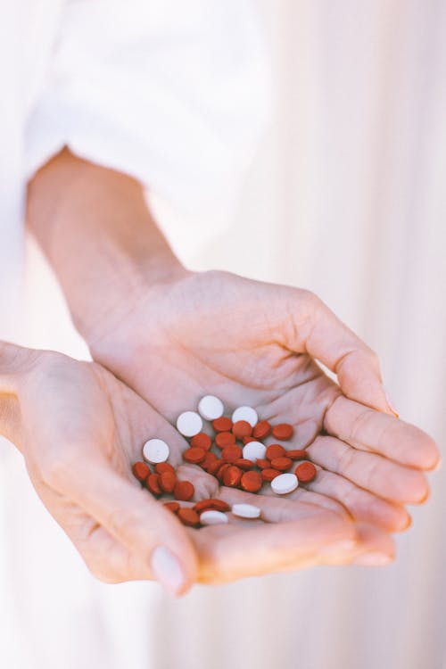 White and Red Round Medication Pill on Persons Hands