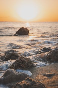Peaceful sunrise over ocean waves and rocks on a sandy beach. Ideal for travel and nature themes.