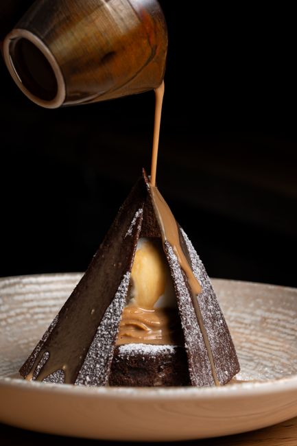 A two-layer caramel cake on a cake stand with thick caramel frosting on top and sides, one slice cut to show the tender crumb inside.