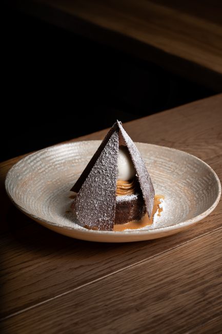 A bowl of fluffy white powdered sugar frosting with a rubber spatula lifting a swirl, next to a partially frosted layer cake.