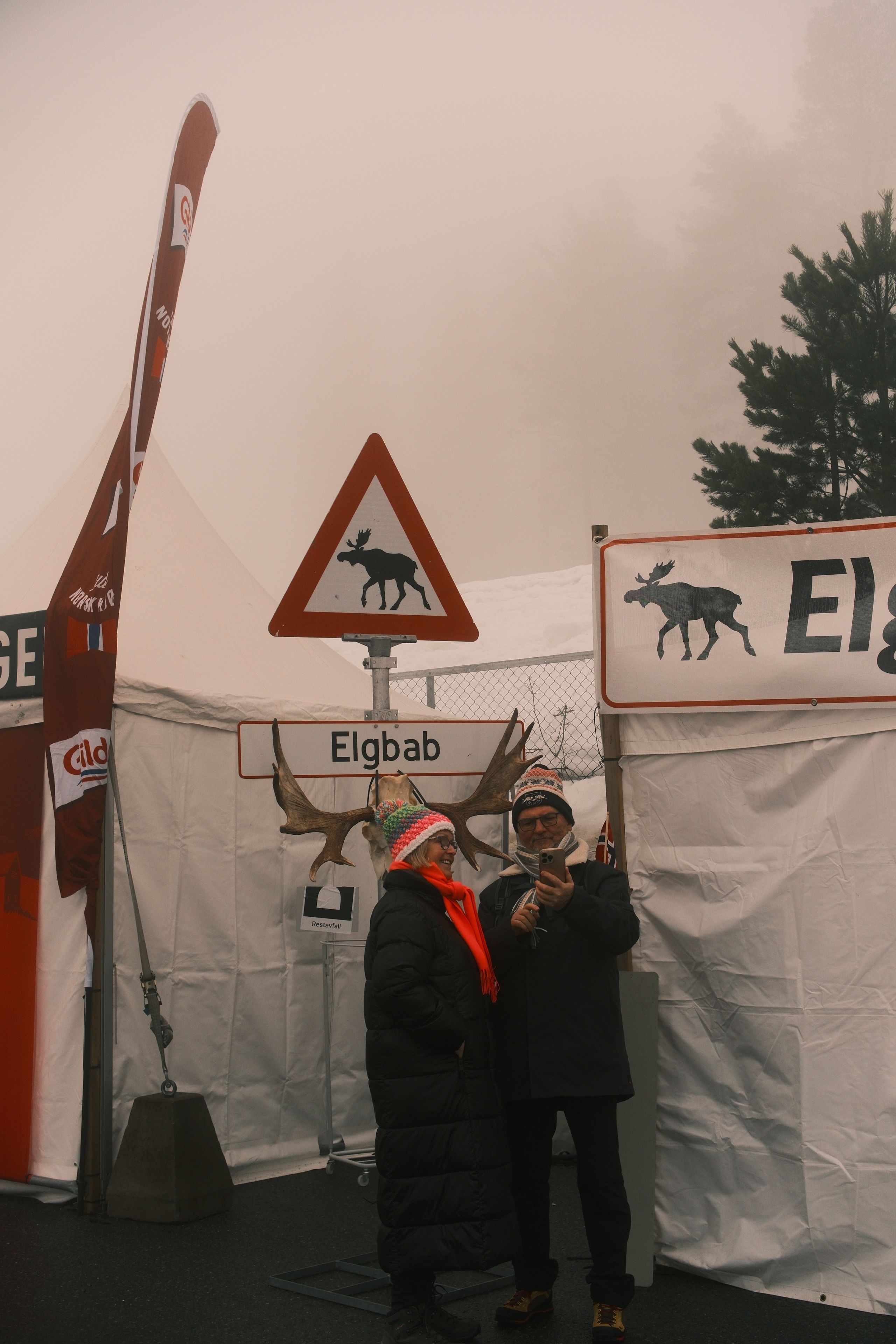 Couple at a winter fair with moose-themed signage in a foggy setting. Captured with X-T5 camera.