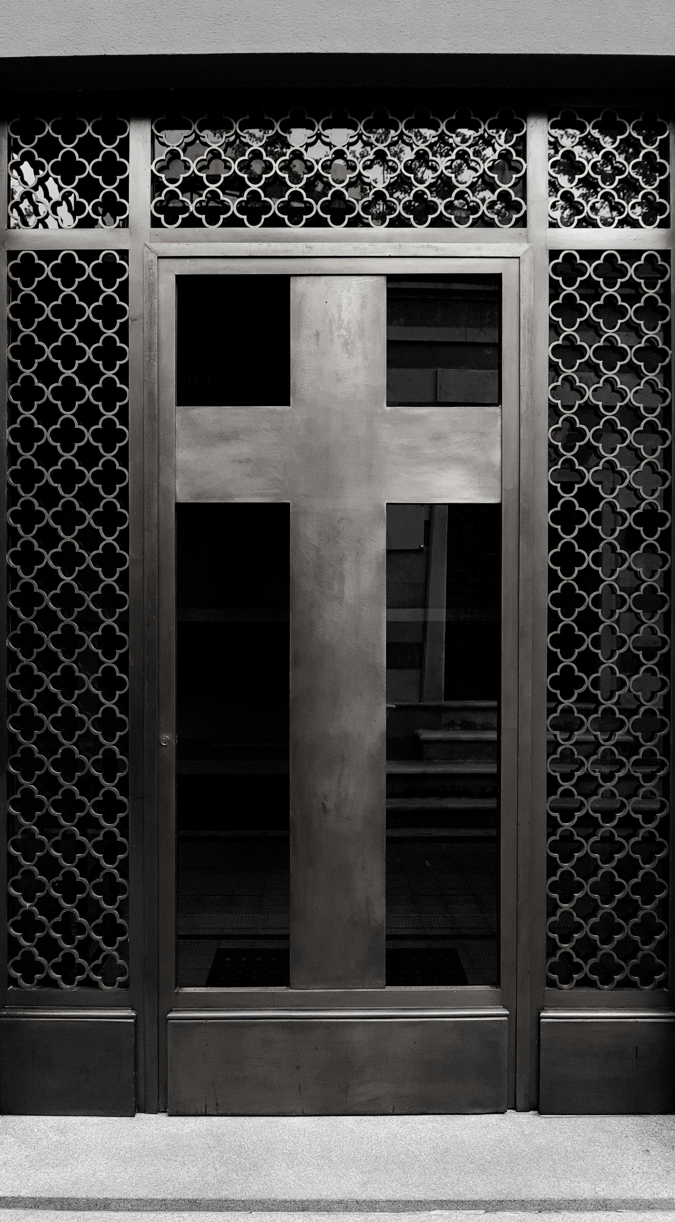 A black and white photo of a metal door with a cross design, symbolizing faith and craftsmanship.