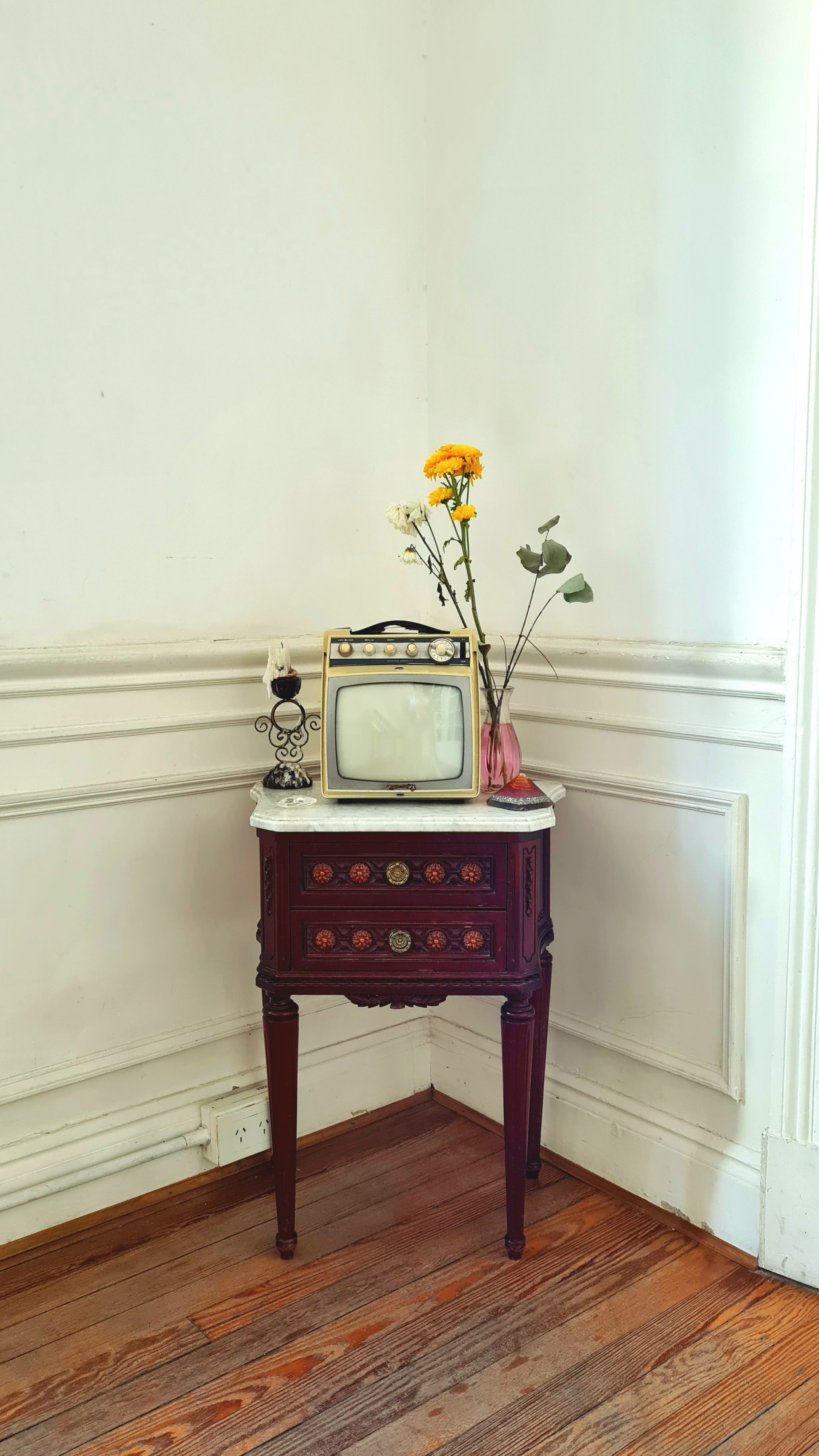 A cozy corner featuring a vintage TV atop a classic wooden side table, accented by a floral arrangement.