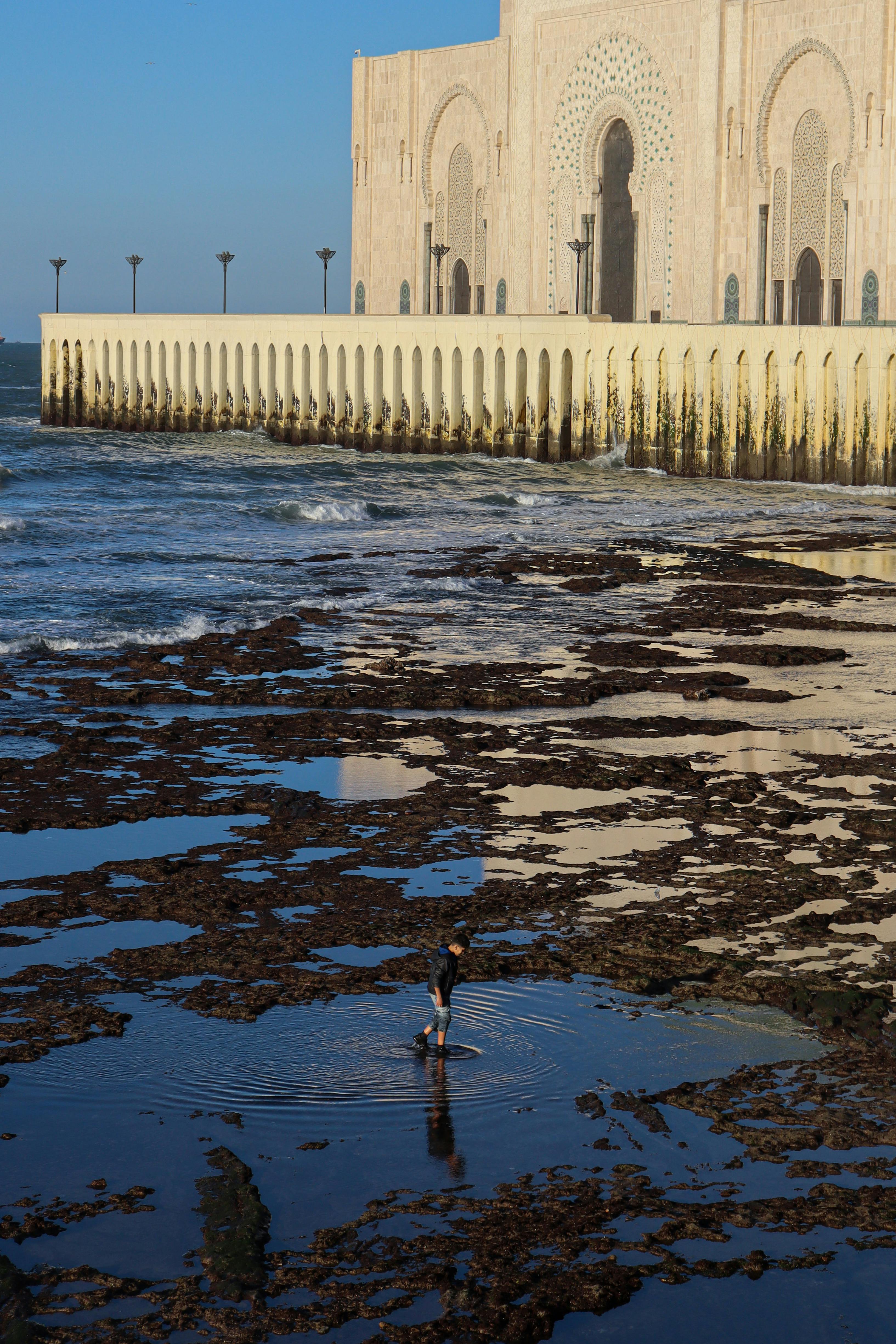 A man walks in tide pools near Casablanca's iconic Hassan II Mosque along the Atlantic coast.