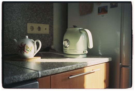 Sunlit kitchen counter with floral teapot and retro kettle, cozy ambiance.