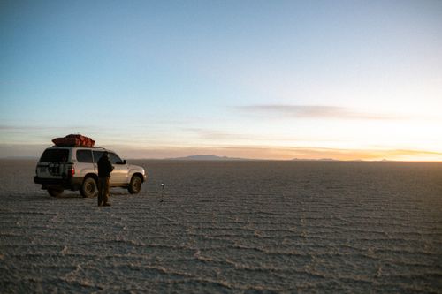 Free Traveler and SUV explore the vast expanse of Bolivia's Salar de Uyuni at sunrise. Stock Photo