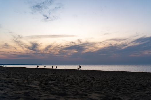 Silhouettes of people walking on Kołobrzeg beach during a stunning sunset.