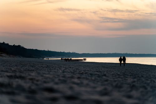 Free A serene sunset view of a couple walking on Kołobrzeg beach, Poland. Stock Photo