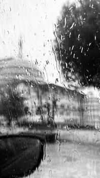 Abstract view through a rainy car window, highlighting water droplets and a blurred cityscape in black and white.