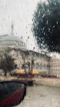 A rainy day with raindrops streaming down a window, blurring the cityscape outside.