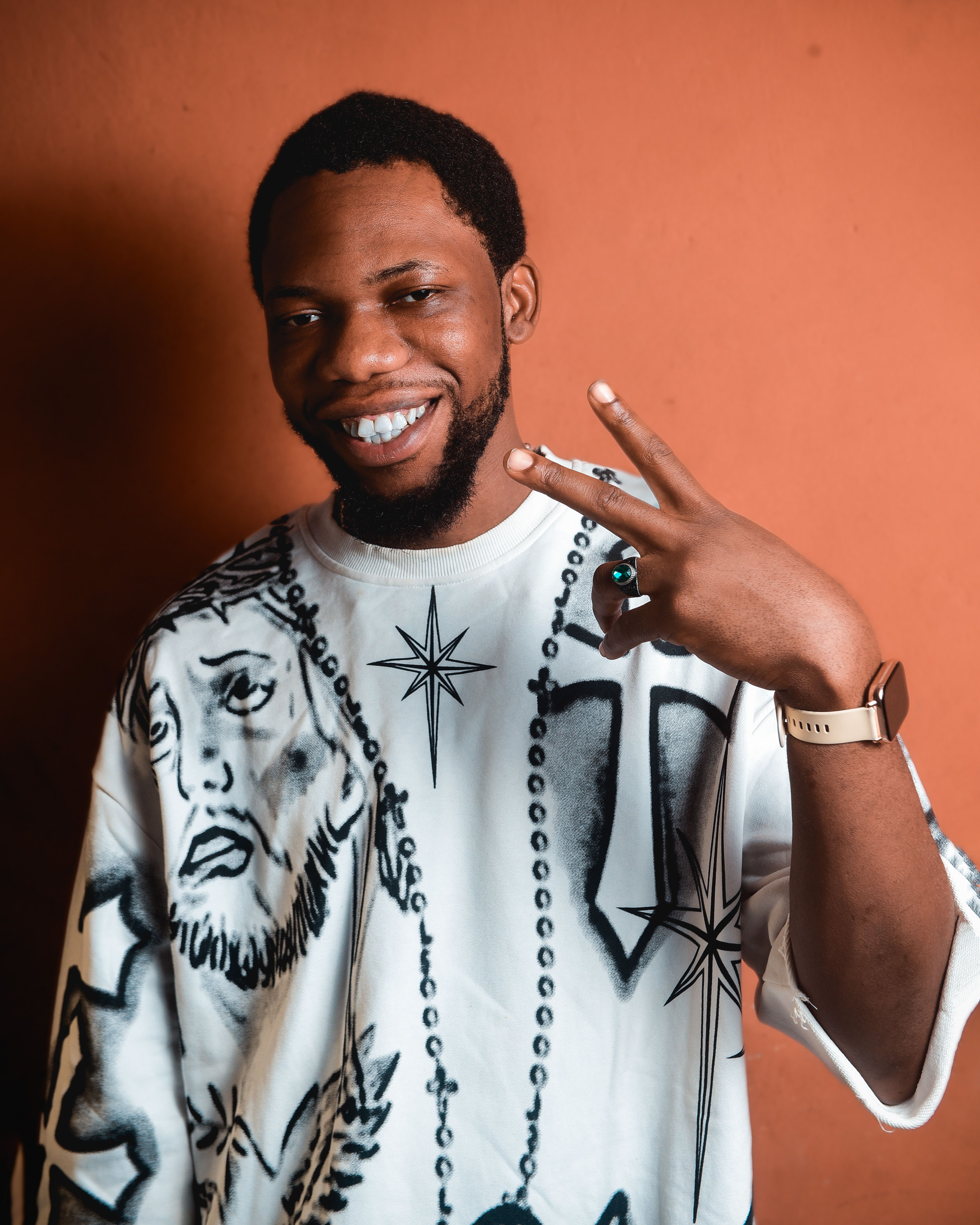 Casual portrait of a smiling man in a graphic tee showing a peace sign gesture.