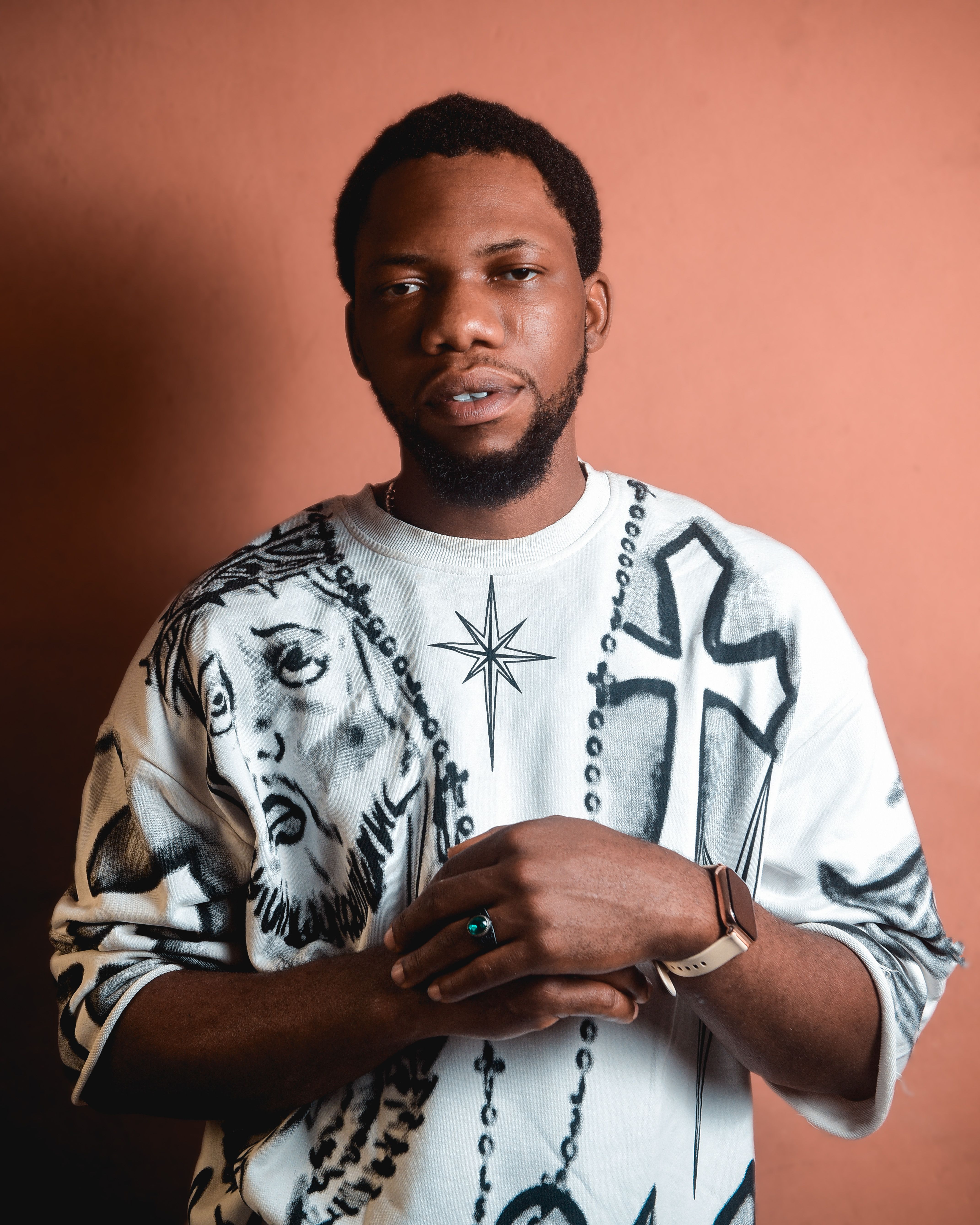 A confident man poses in a creative sweatshirt against a warm backdrop.