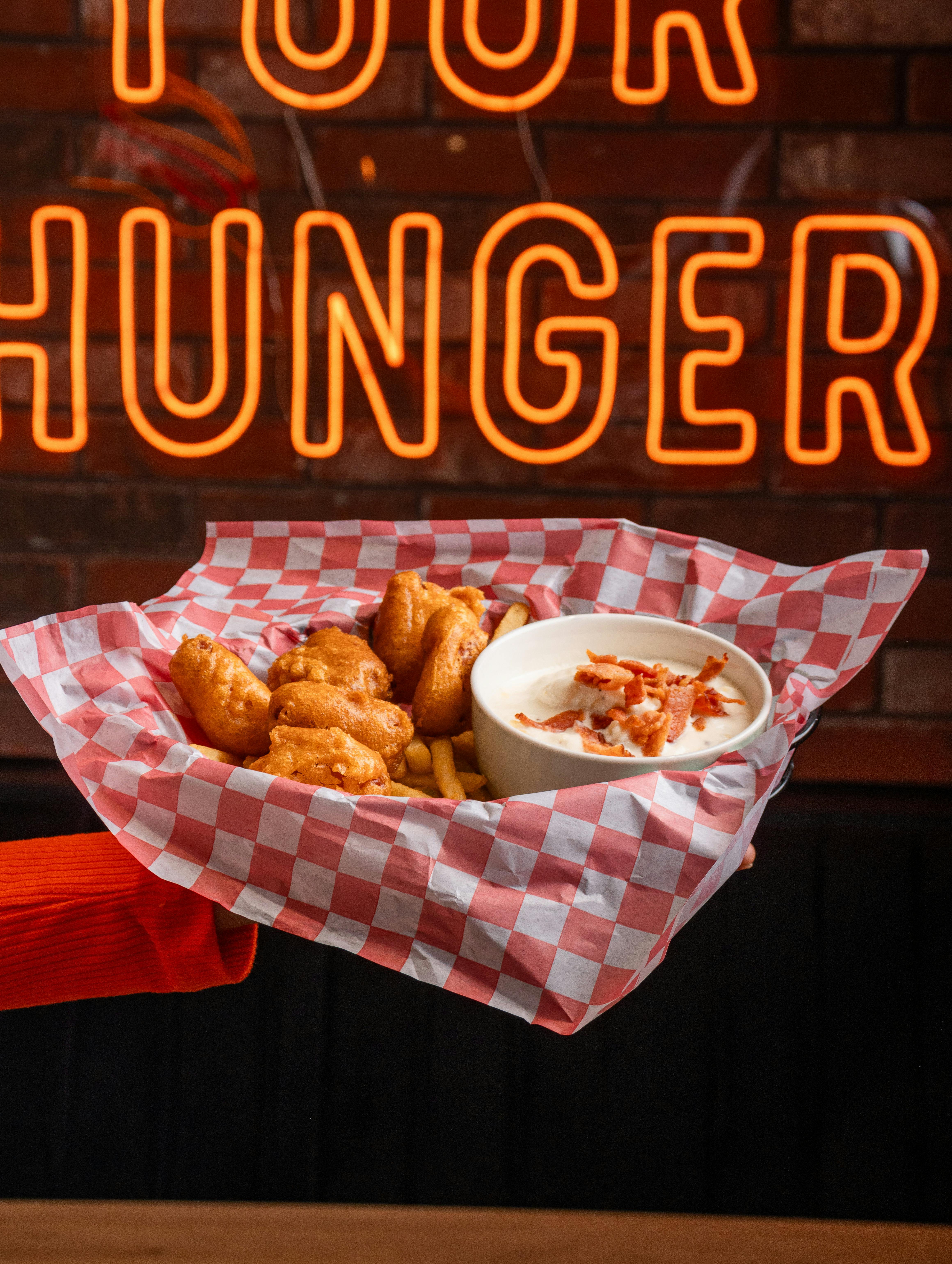 A basket of fried food with dip held against a neon sign. Perfect for food promotions.