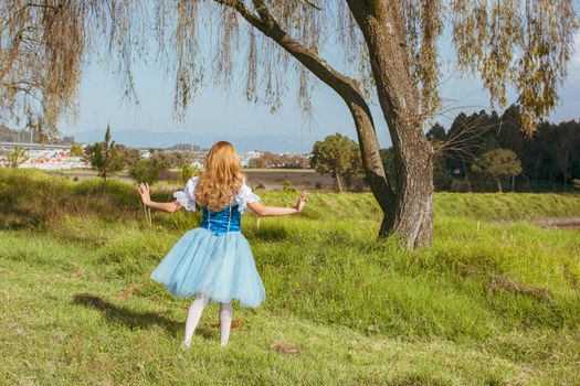 A young woman in a blue dress embracing nature in a sunny outdoor setting.