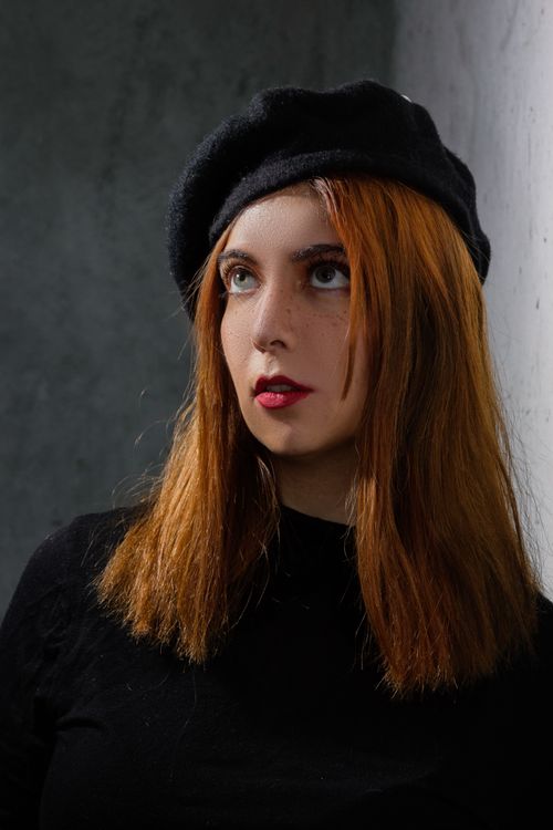 Free Stylish portrait of a redhead woman with freckles in a black beret and top against a gray background. Stock Photo