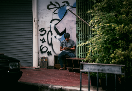 Casual moment on a Bangkok street with a man using his smartphone, graffiti backdrop.
