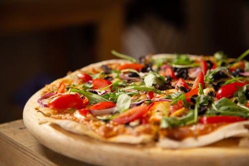 Free Close-up of a fresh vegetable pizza topped with arugula and cherry tomatoes on a wooden board. Stock Photo